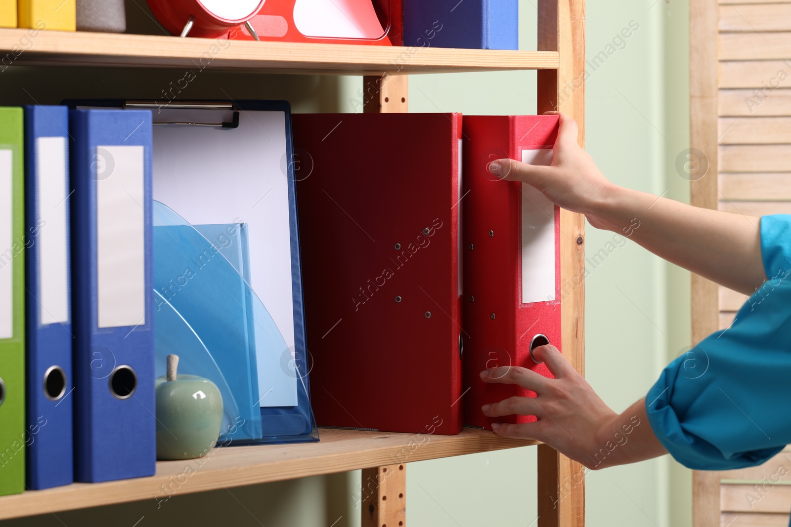 Photo of Woman taking binder office folder from shelving unit indoors, closeup