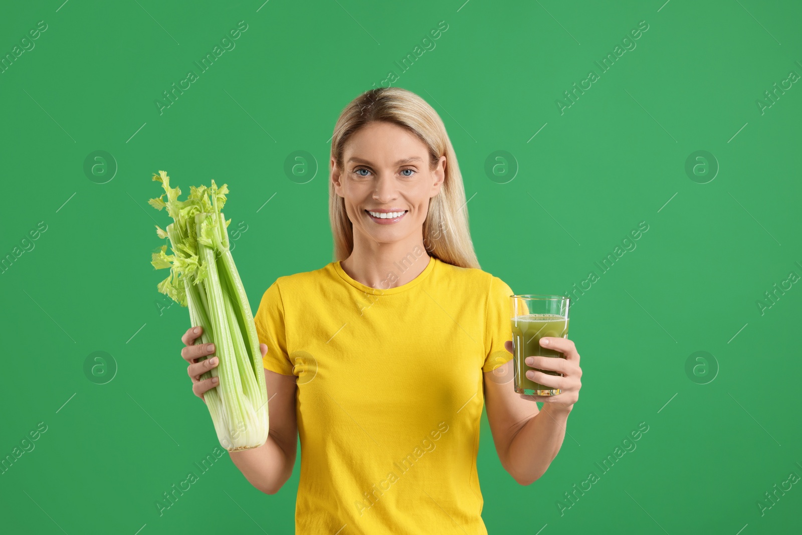 Photo of Happy woman with glass of tasty celery juice and fresh vegetable on green background