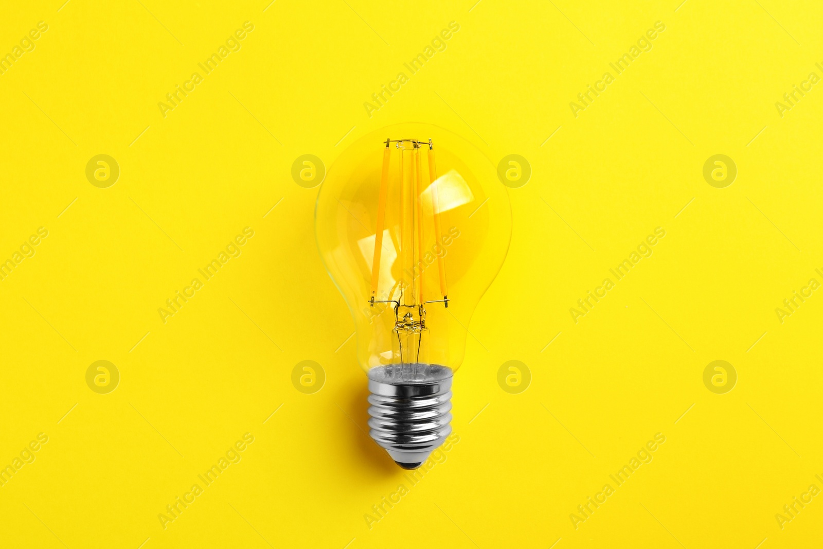 Photo of Vintage filament lamp bulb on yellow background, top view