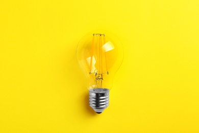 Vintage filament lamp bulb on yellow background, top view