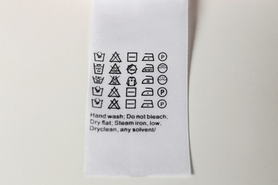 Clothing label with care symbols on white background, top view