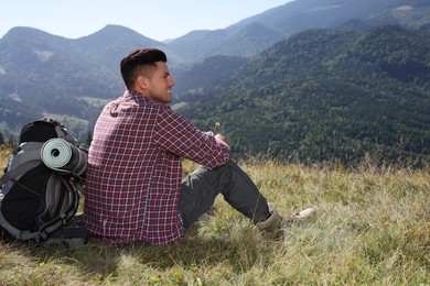 Photo of Tourist with backpack sitting on ground and enjoying view in mountains