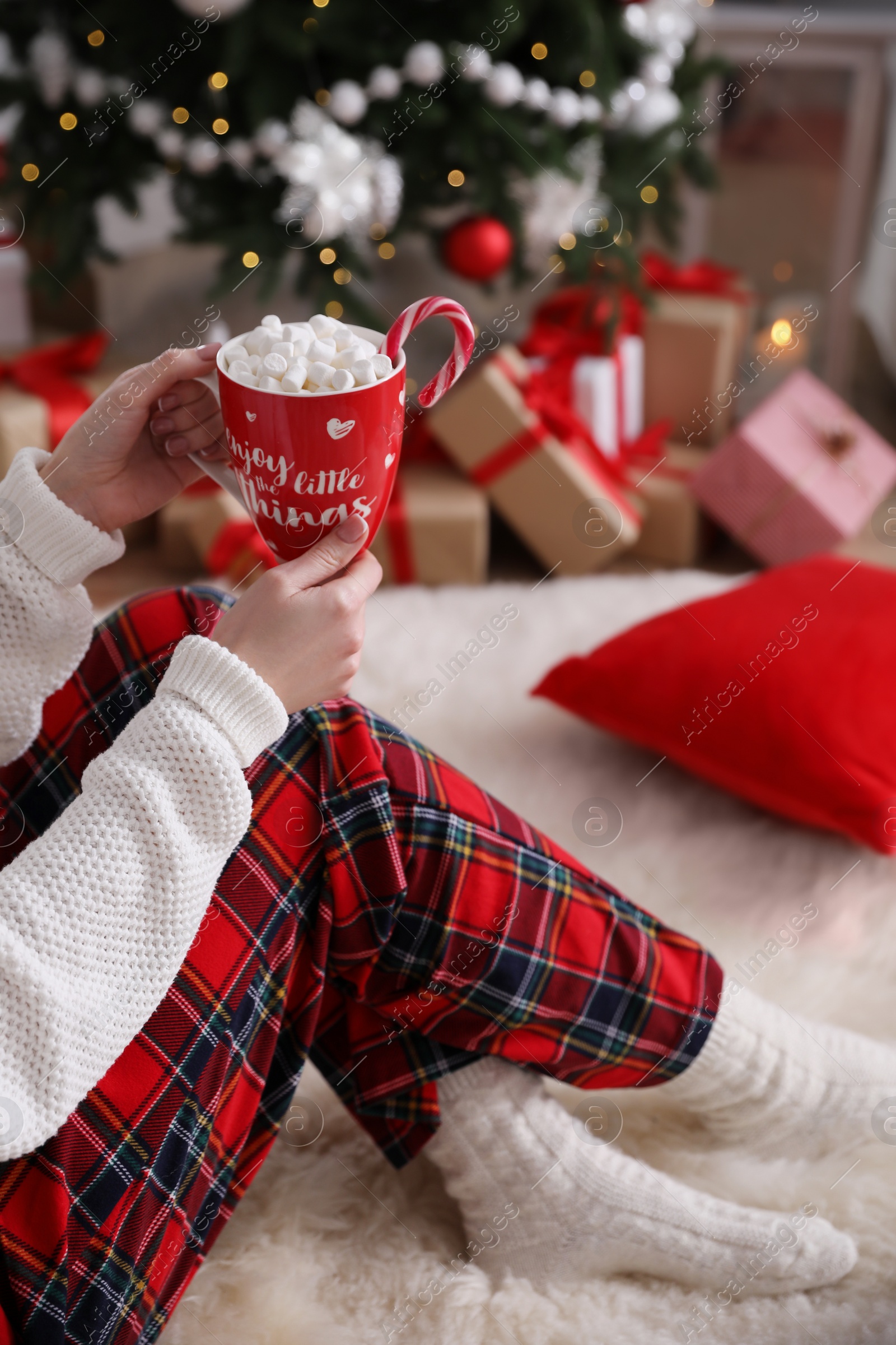 Photo of Woman with cup of delicious hot drink near Christmas tree at home, closeup