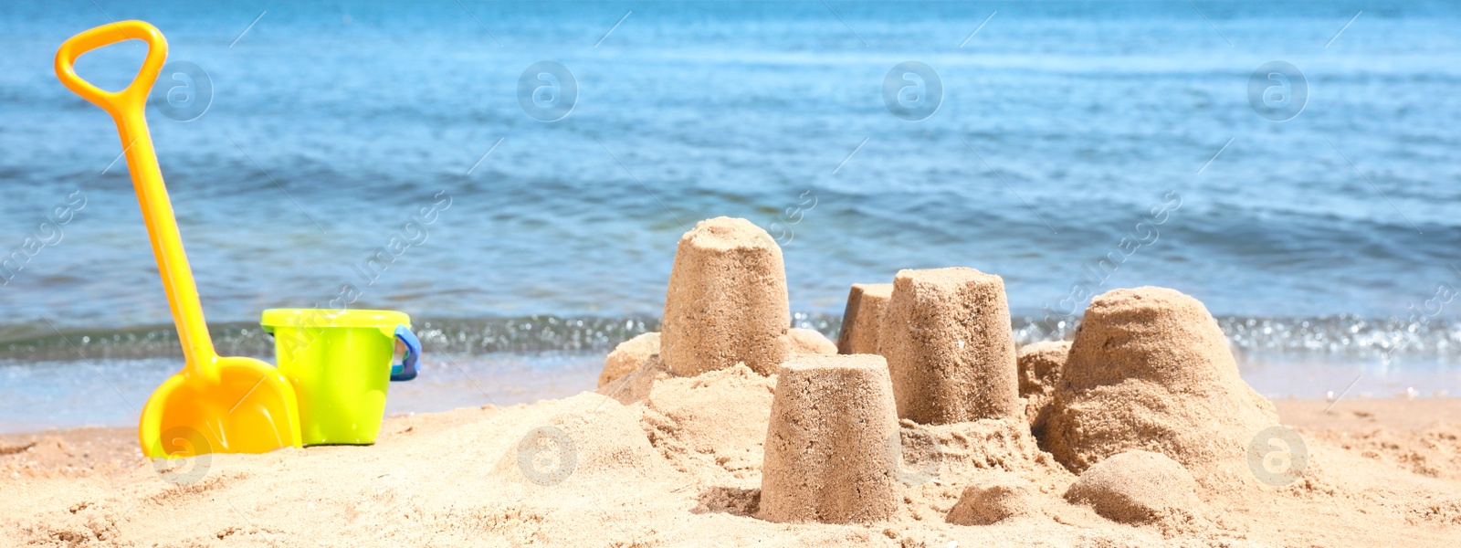 Image of Little sand figures and plastic toys on beach near sea. Banner design