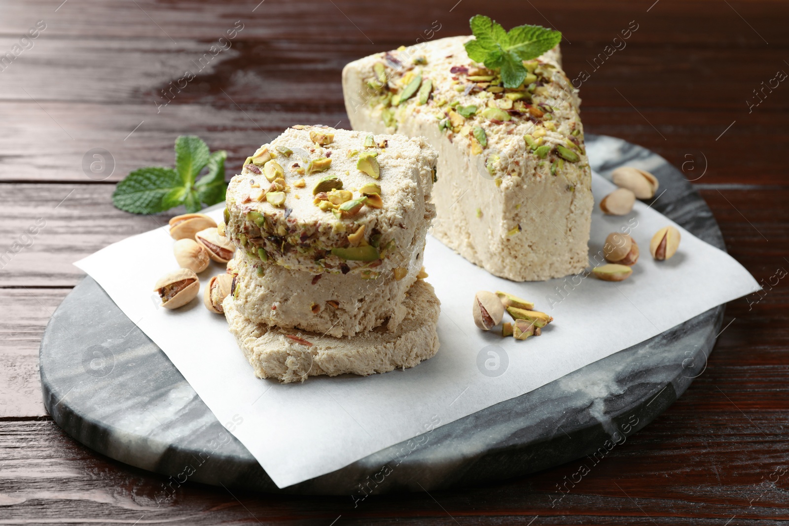 Photo of Pieces of tasty halva with pistachios and mint on wooden table, closeup