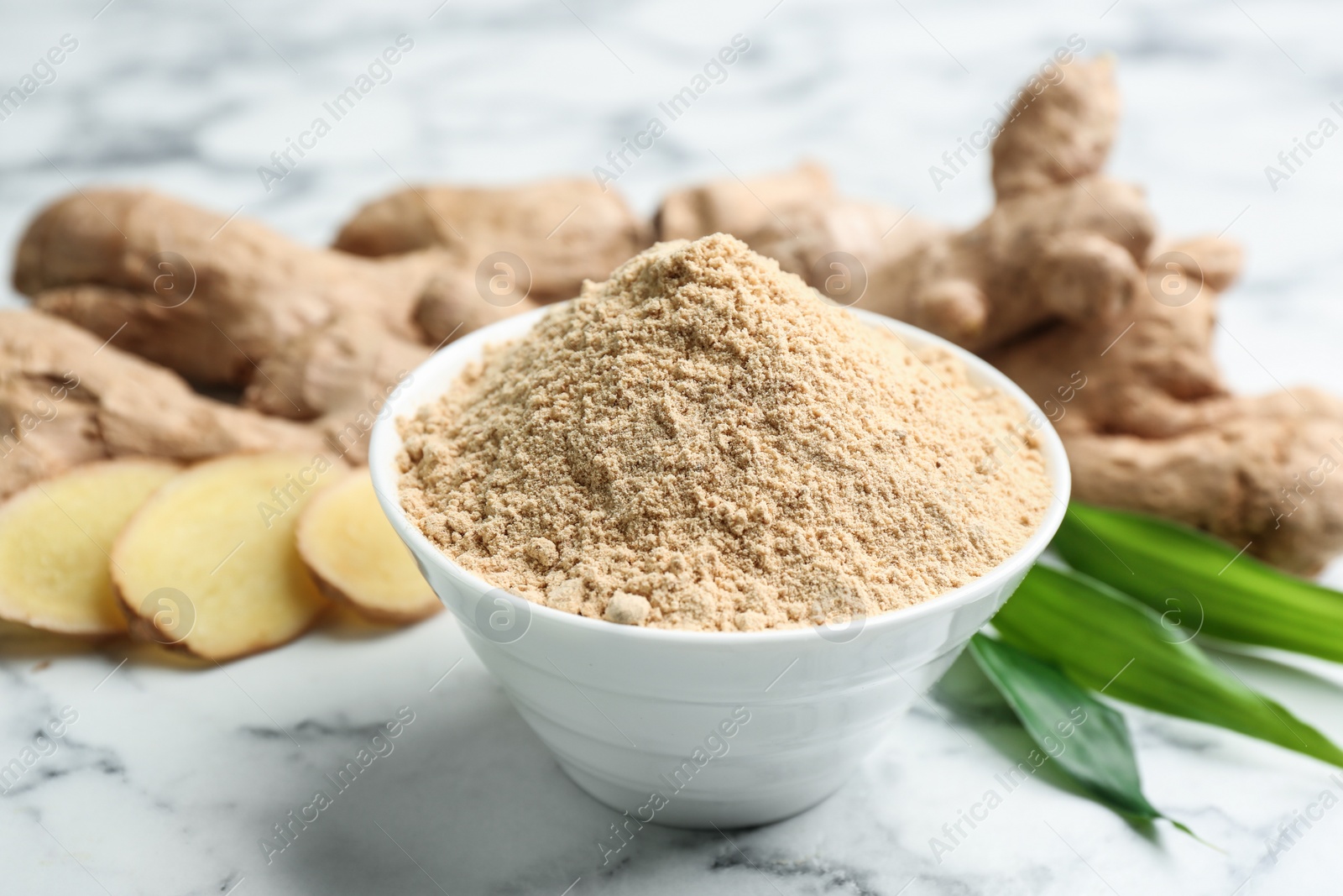 Photo of Dry ginger powder, fresh root and leaves on white marble table