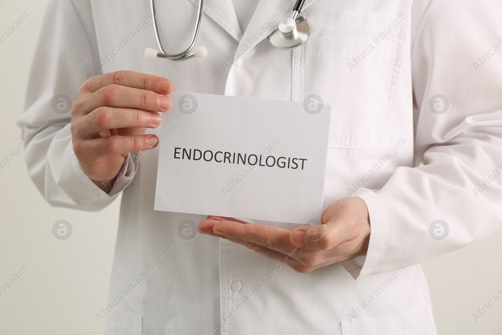 Image of Endocrinologist with stethoscope holding card on light grey background, closeup