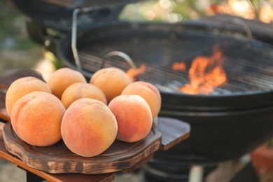 Photo of Fresh peaches on wooden board near modern grill outdoors, closeup