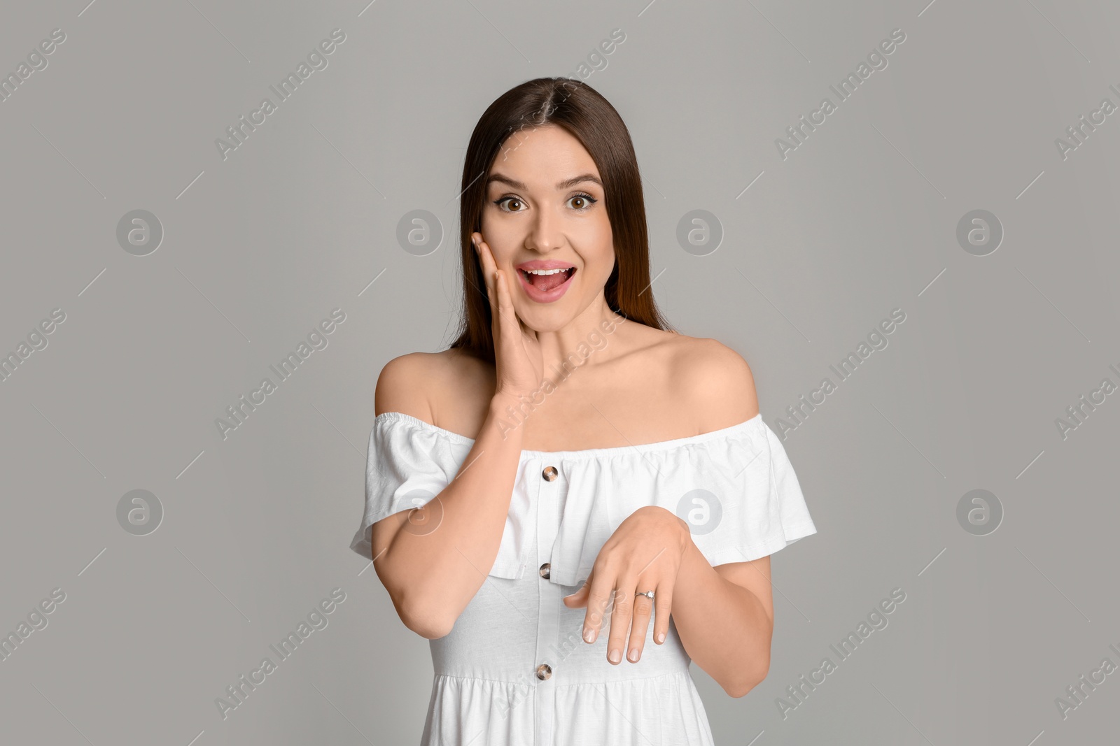 Photo of Emotional young woman wearing beautiful engagement ring on grey background