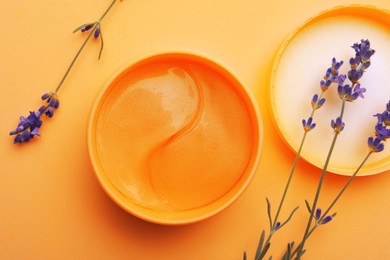 Package of under eye patches and lavender flowers on orange background, flat lay. Cosmetic product