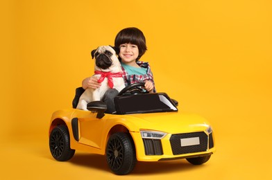 Photo of Little boy with his dog in toy car on yellow background