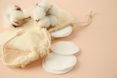 Photo of Bags with cotton pads and flowers on beige background, closeup. Space for text