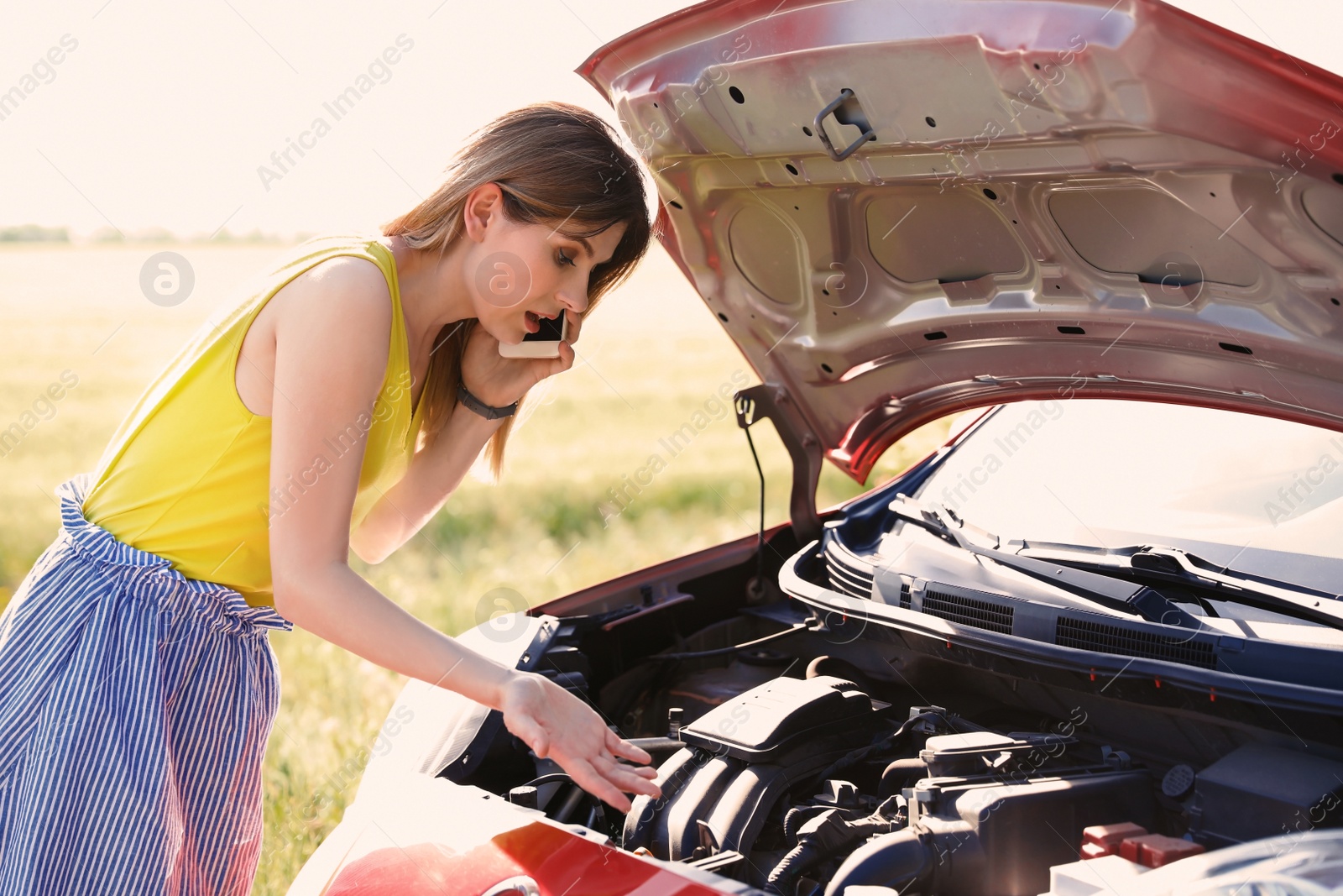 Photo of Stressed woman with mobile phone standing near broken car in countryside