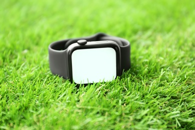Photo of Modern stylish smart watch on green grass, closeup