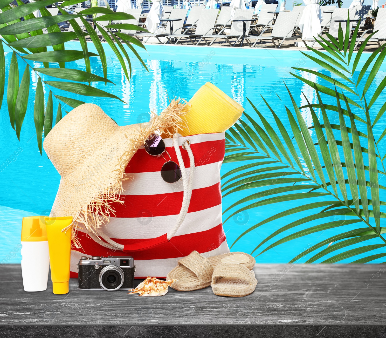 Image of Stylish bag with beach accessories and camera on grey stone surface near outdoor swimming pool