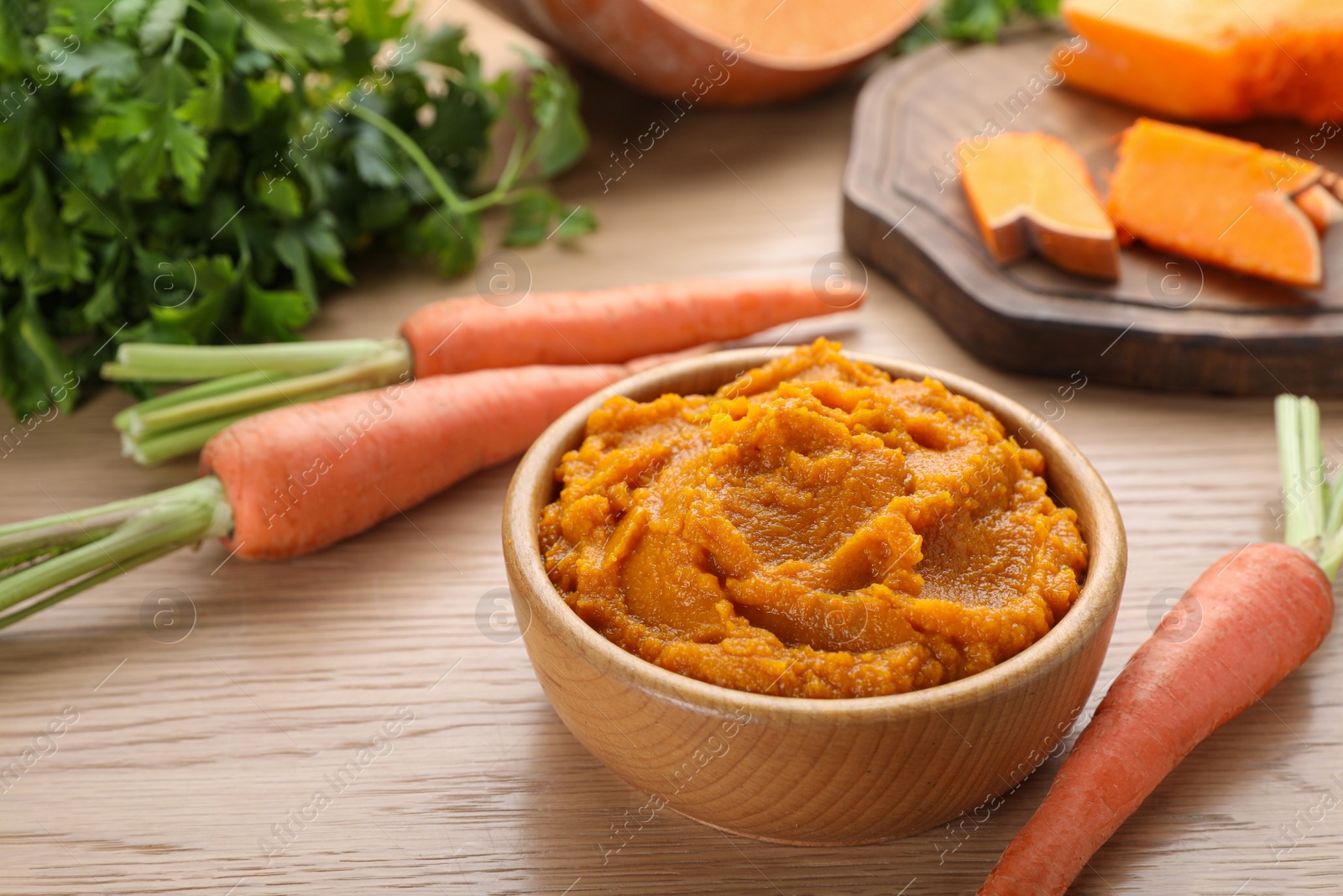 Photo of Bowl with tasty orange puree and ingredients on wooden table