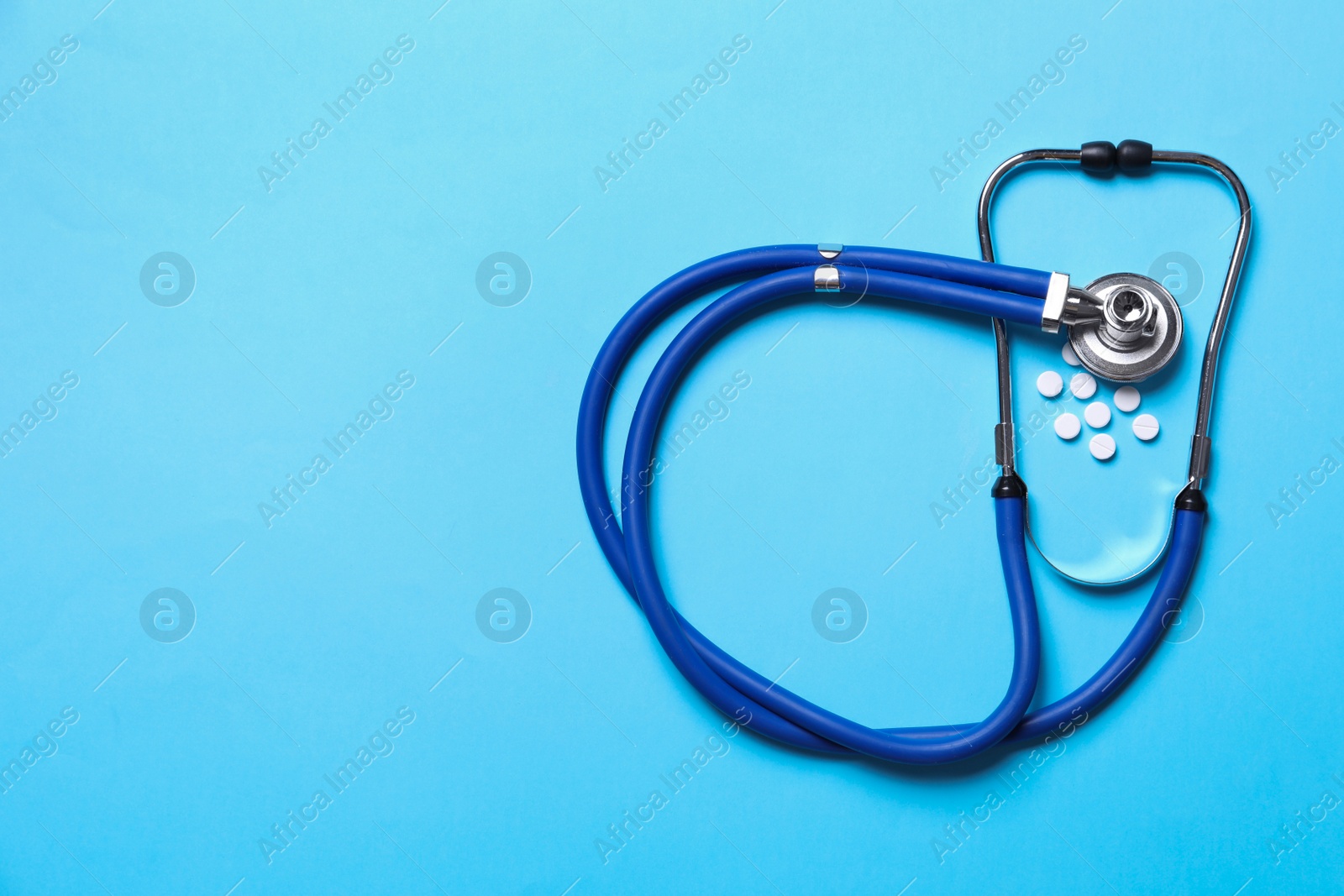 Photo of Stethoscope and pills on light blue background, flat lay. Space for text