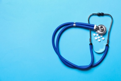 Photo of Stethoscope and pills on light blue background, flat lay. Space for text