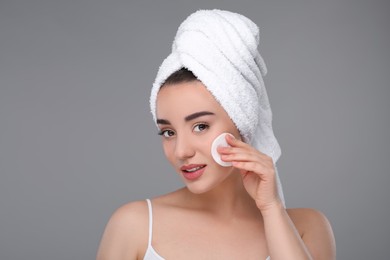 Beautiful woman in terry towel removing makeup with cotton pad on gray background