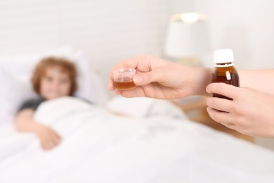 Photo of Mother with cough syrup for her son in bedroom, focus on hands