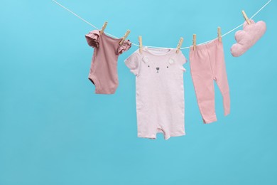 Different baby clothes and cloud shaped pillow drying on laundry line against light blue background. Space for text