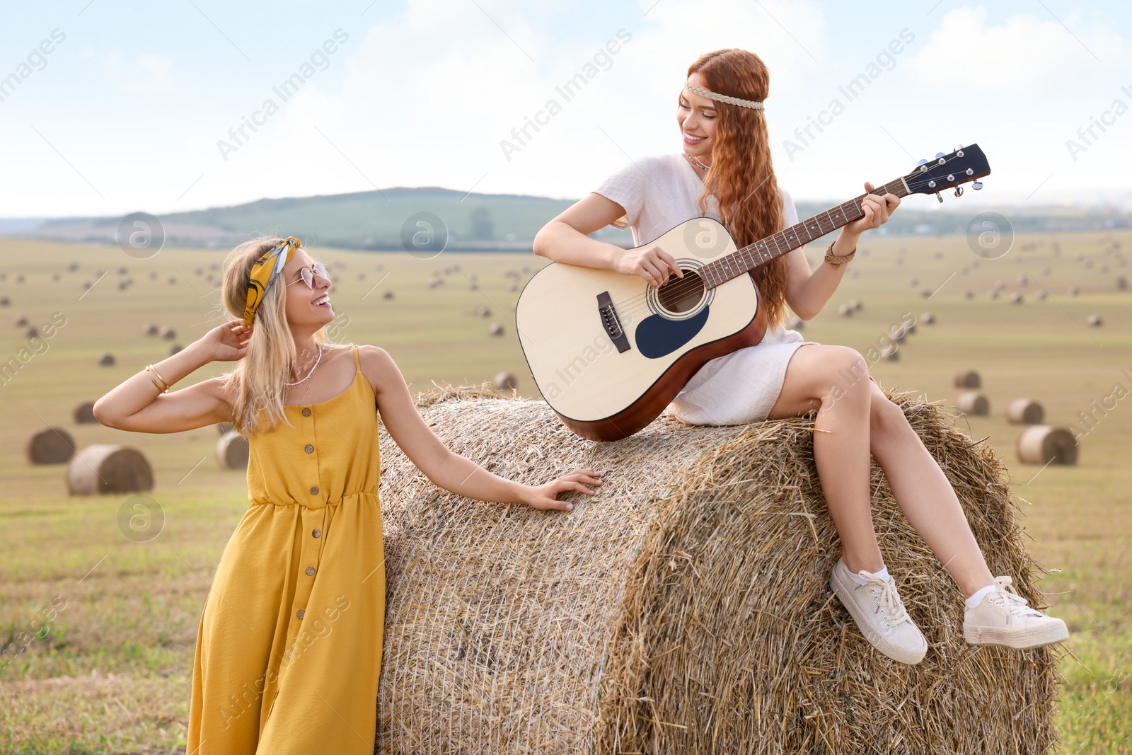 Photo of Beautiful hippie woman listening to her friend playing guitar in field