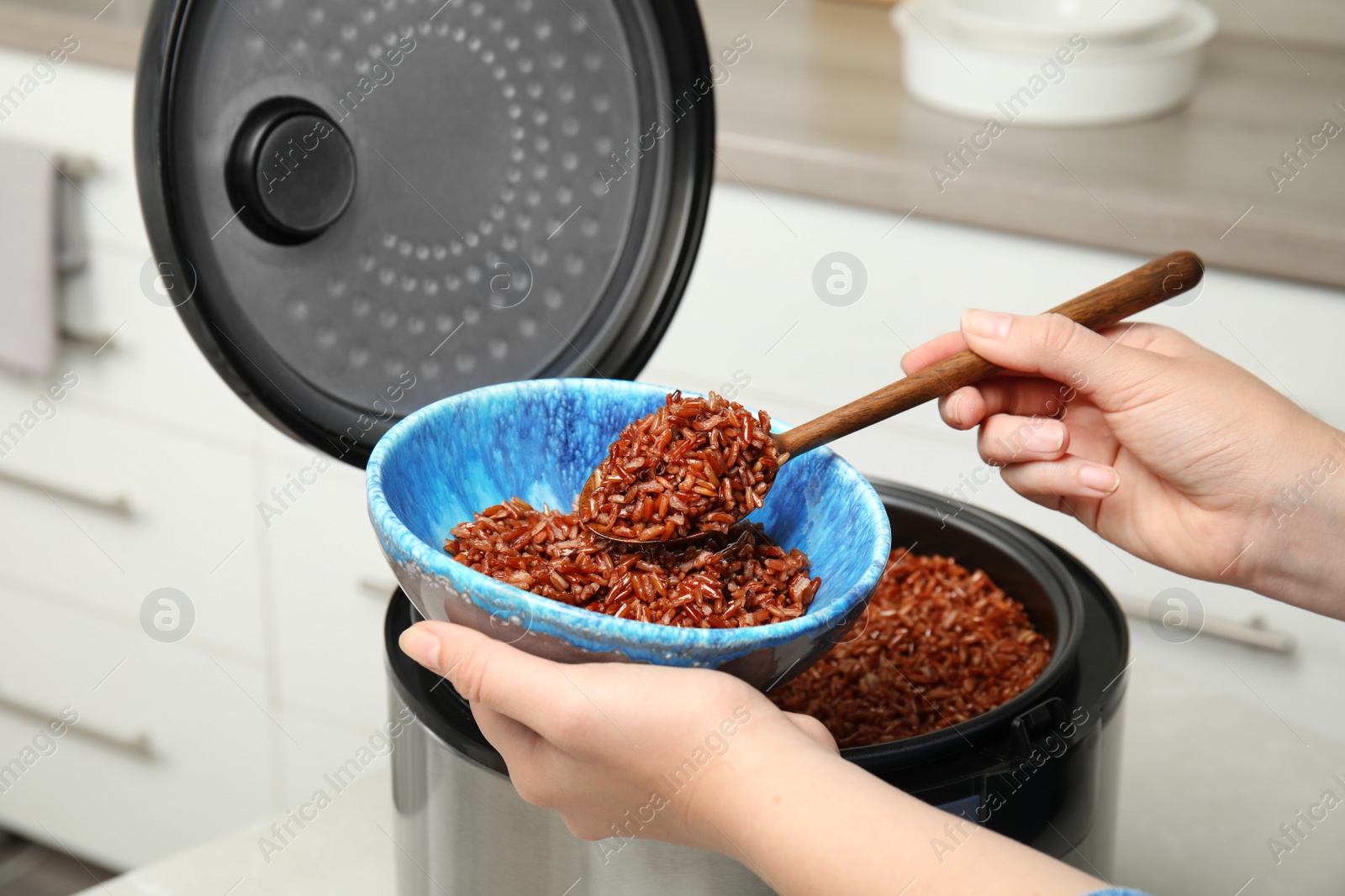 Photo of Woman putting delicious brown rice into bowl from multi cooker, closeup