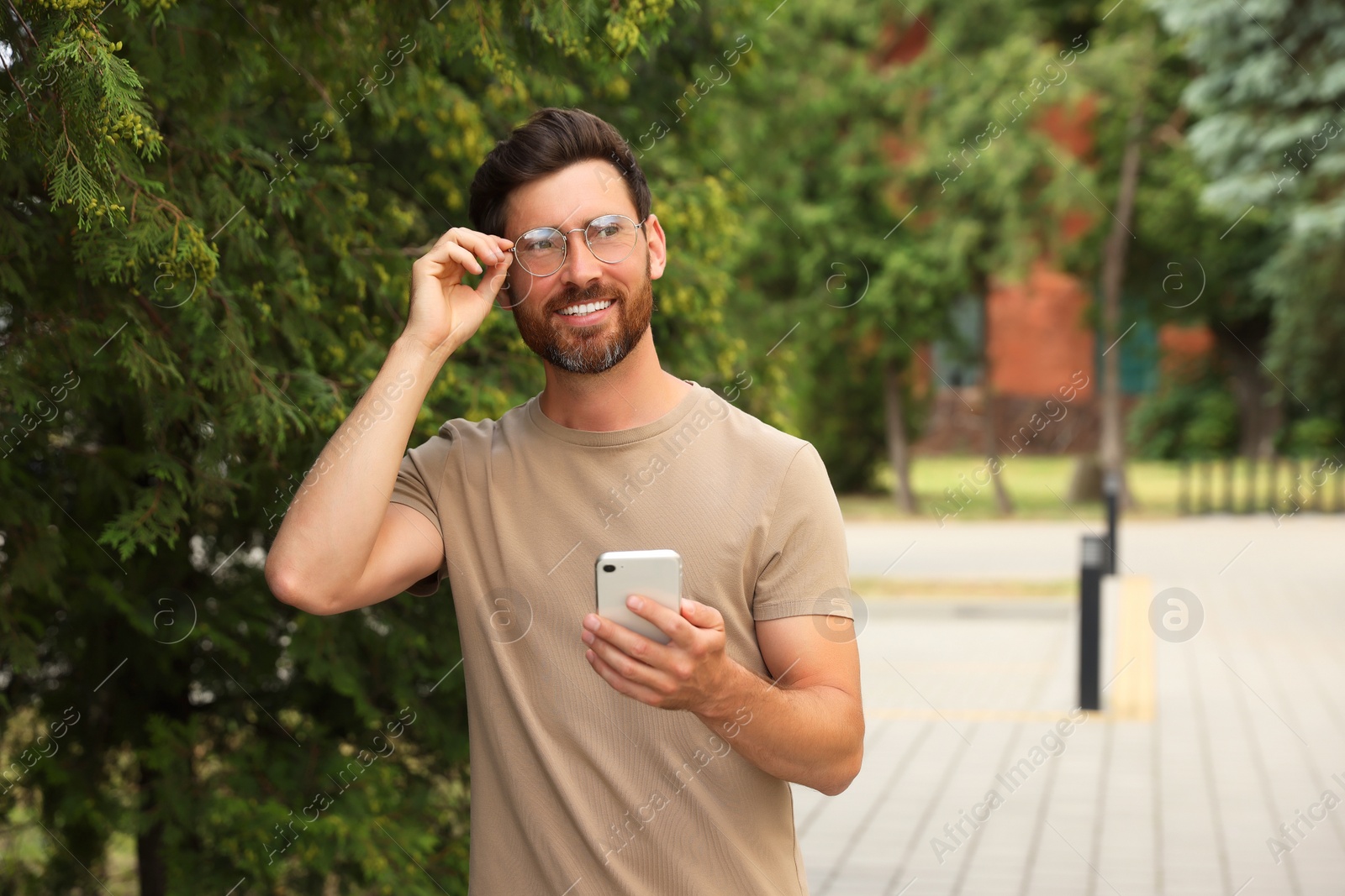 Photo of Smiling handsome bearded man with smartphone outdoors. Space for text