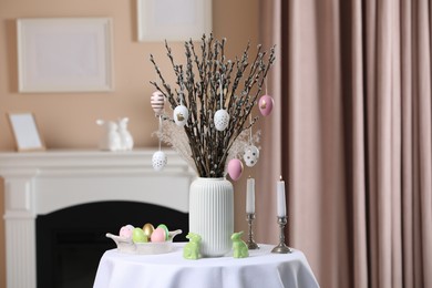 Pussy willow branches with festively decorated eggs, Easter bunnies and candles on table indoors