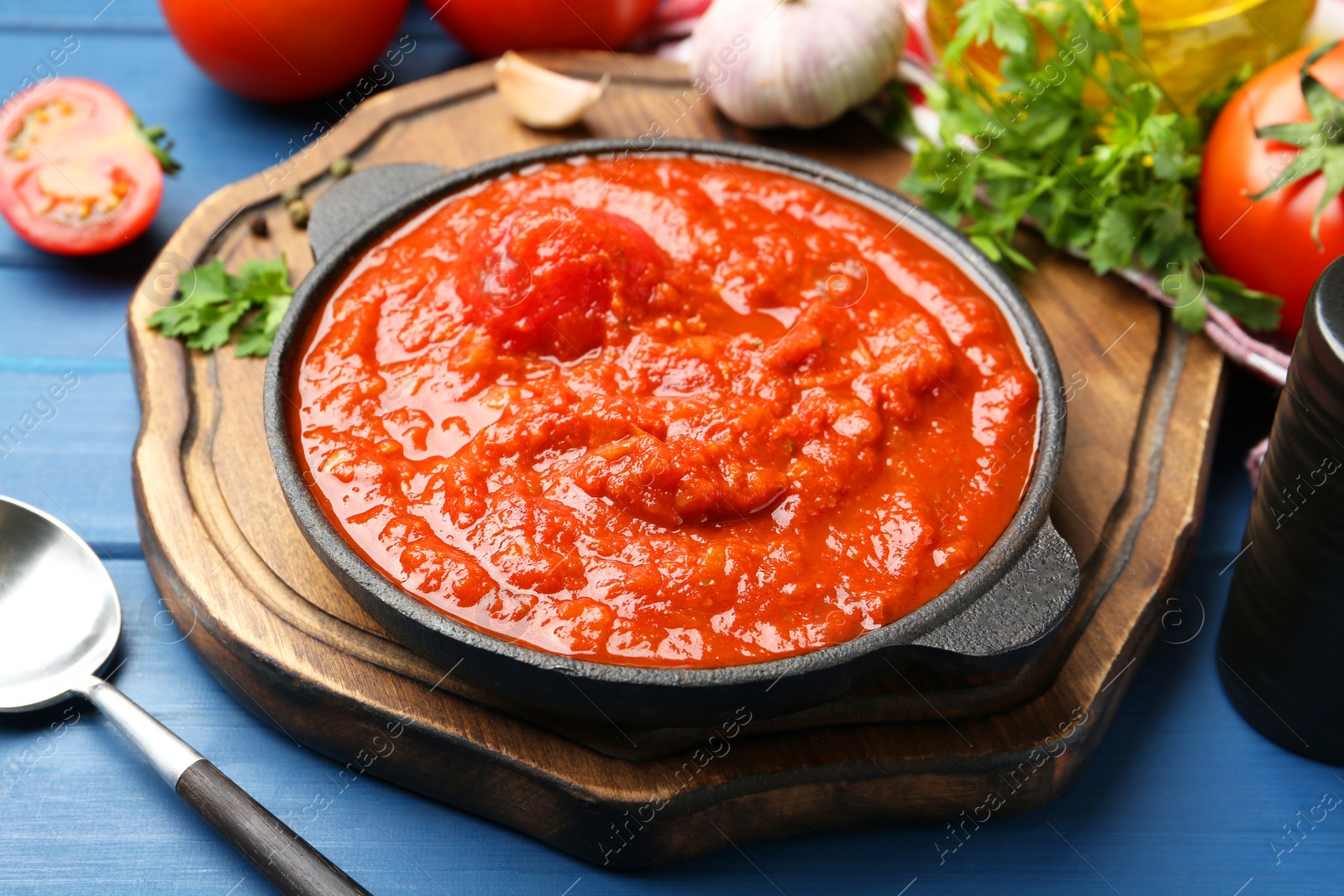 Photo of Homemade tomato sauce in bowl, spoon and ingredients on blue wooden table