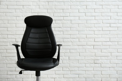 Comfortable office chair near white brick wall. Space for text