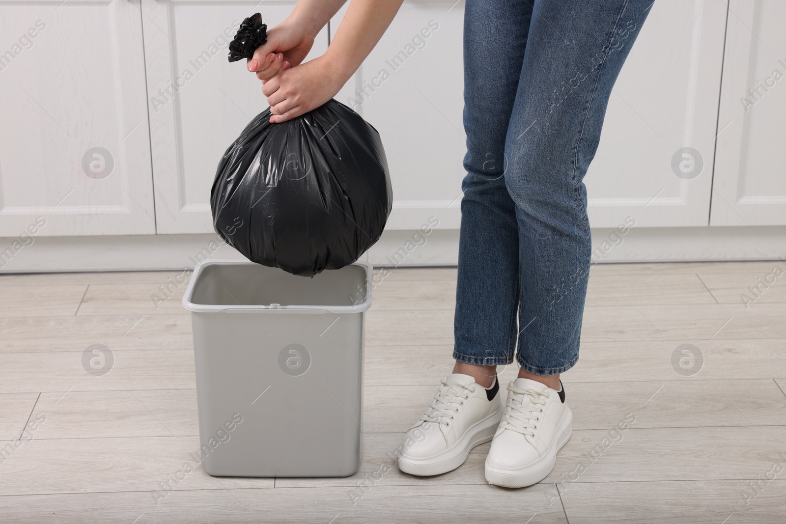 Photo of Woman taking garbage bag out of trash bin in kitchen, closeup