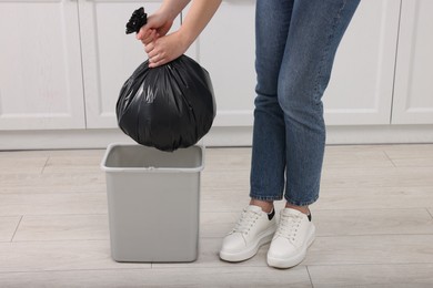 Photo of Woman taking garbage bag out of trash bin in kitchen, closeup