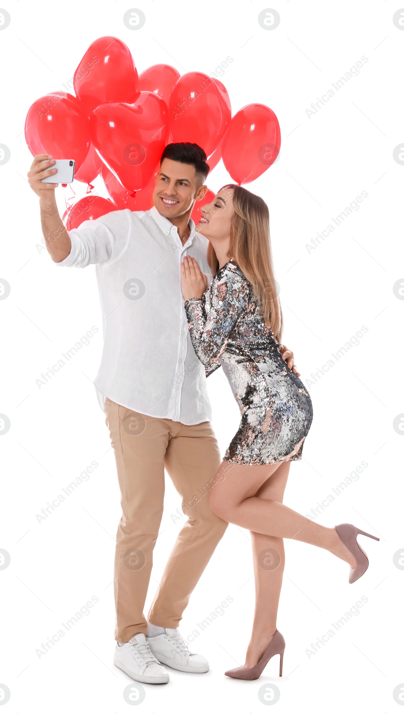 Photo of Lovely couple with heart shaped balloons taking selfie on white background. Valentine's day celebration