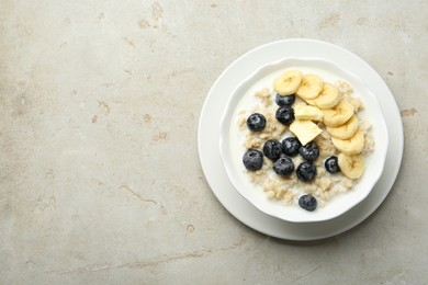 Tasty oatmeal with banana, blueberries, butter and milk served in bowl on light grey table, top view. Space for text