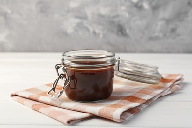Tasty barbecue sauce in glass jar on white wooden table