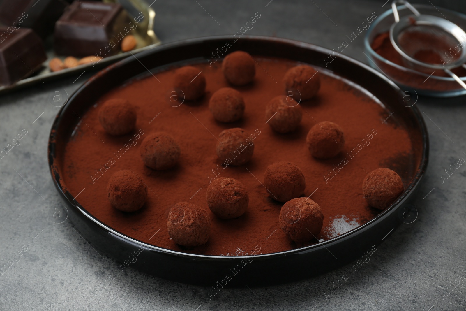 Photo of Delicious chocolate candies powdered with cocoa on grey table