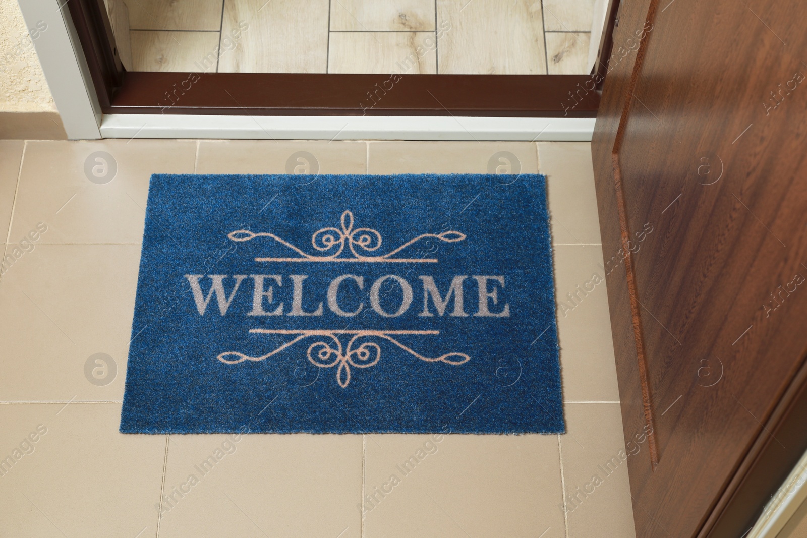 Photo of Beautiful blue doormat with word Welcome on floor near entrance, above view