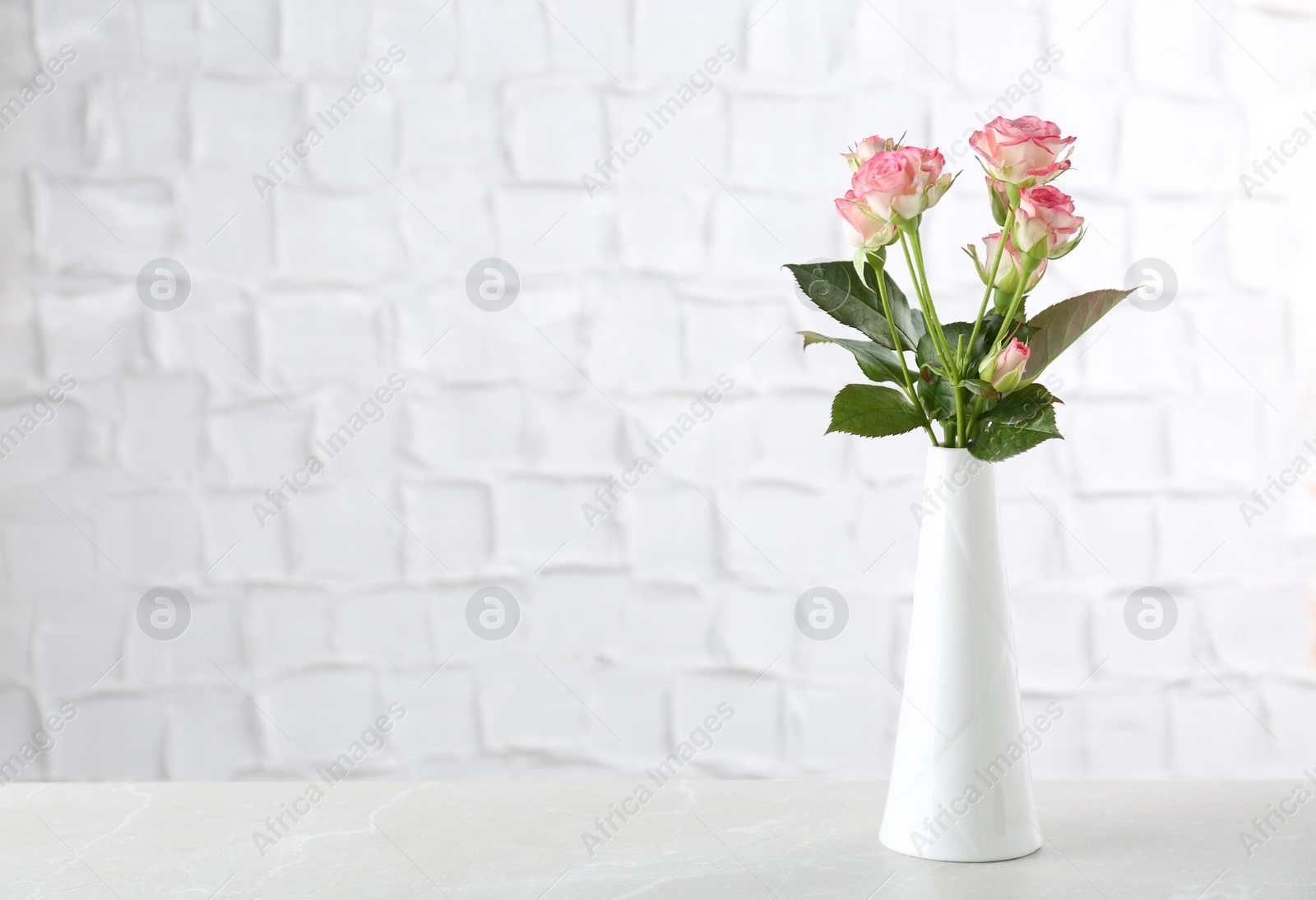 Photo of Vase with beautiful pink roses on white table near brick wall