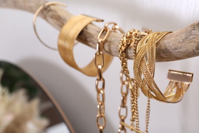 Photo of Beautiful bracelets and necklaces on wooden branch indoors, closeup