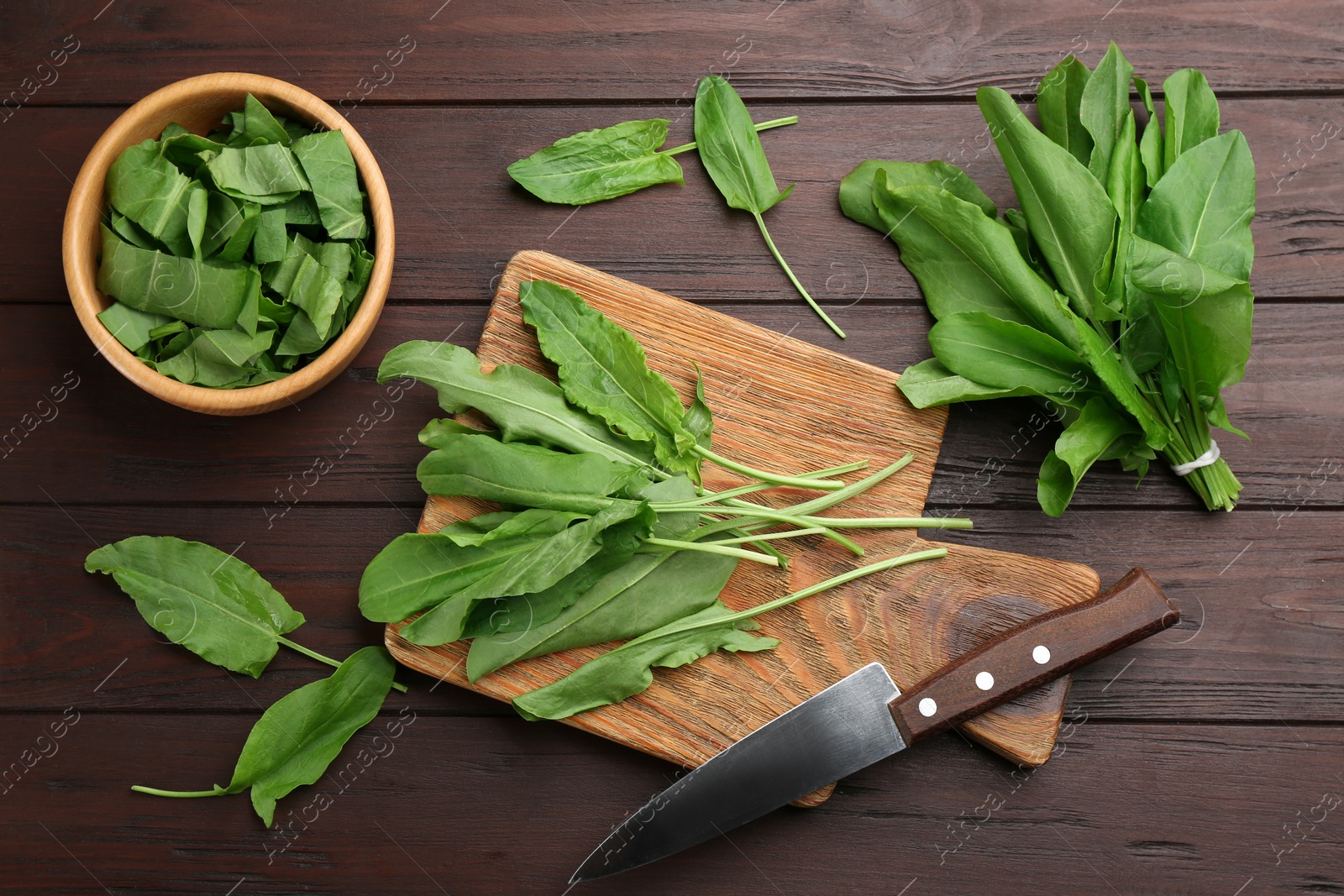 Photo of Fresh green sorrel leaves and knife on brown wooden table, flat lay