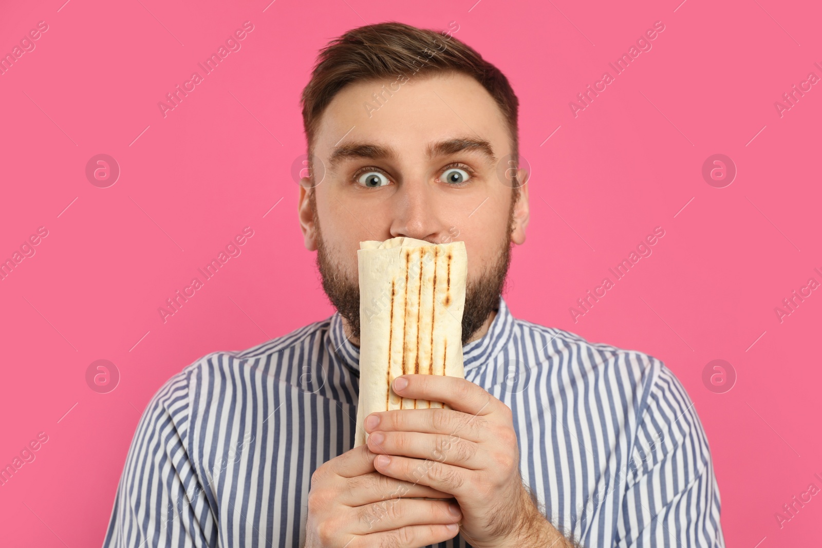 Photo of Emotional young man with delicious shawarma on pink background