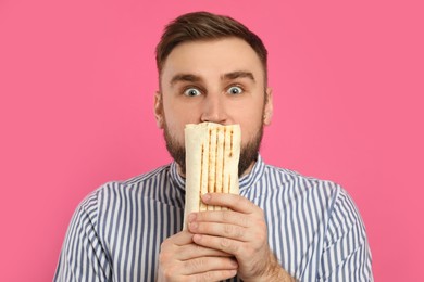Emotional young man with delicious shawarma on pink background