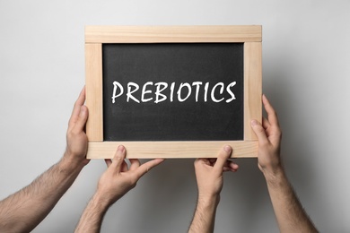 Image of Men holding chalkboard with word PREBIOTICS on light background, closeup 