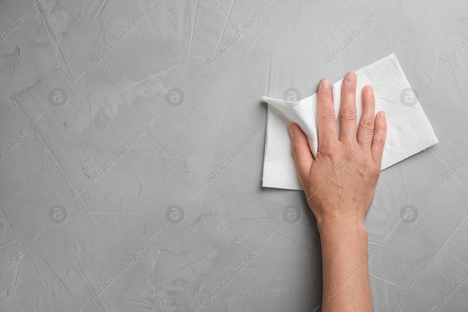 Photo of Woman wiping stone surface with paper towel, top view. Space for text