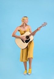 Happy hippie woman playing guitar on light blue background