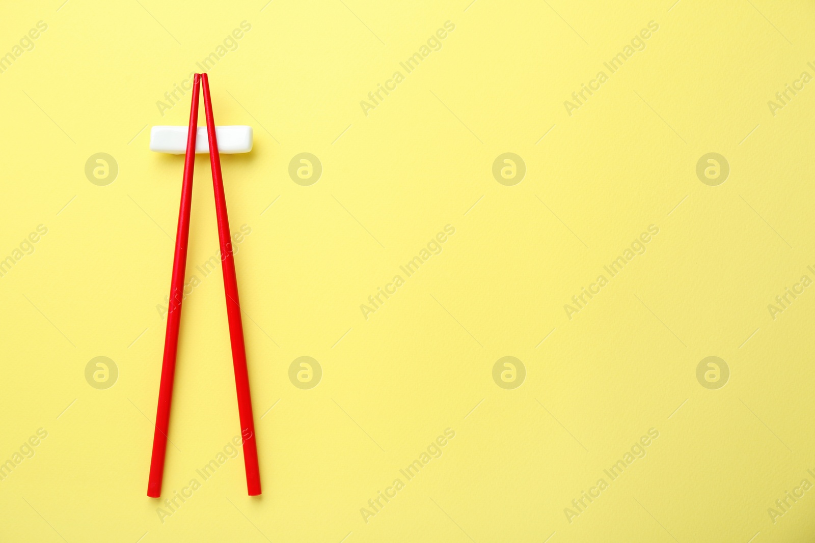 Photo of Pair of red chopsticks with rest on yellow background, top view. Space for text