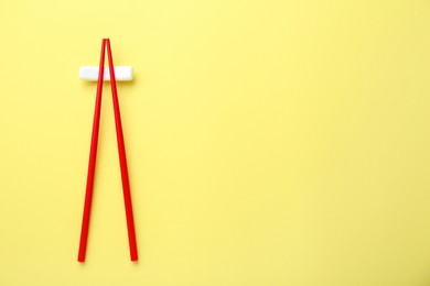 Pair of red chopsticks with rest on yellow background, top view. Space for text