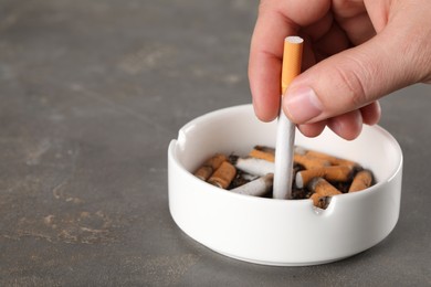 Photo of Man putting out cigarette in ashtray on grey table, closeup. Space for text