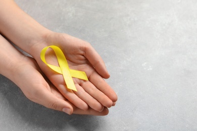 Photo of Woman holding yellow ribbon on grey background. Cancer awareness
